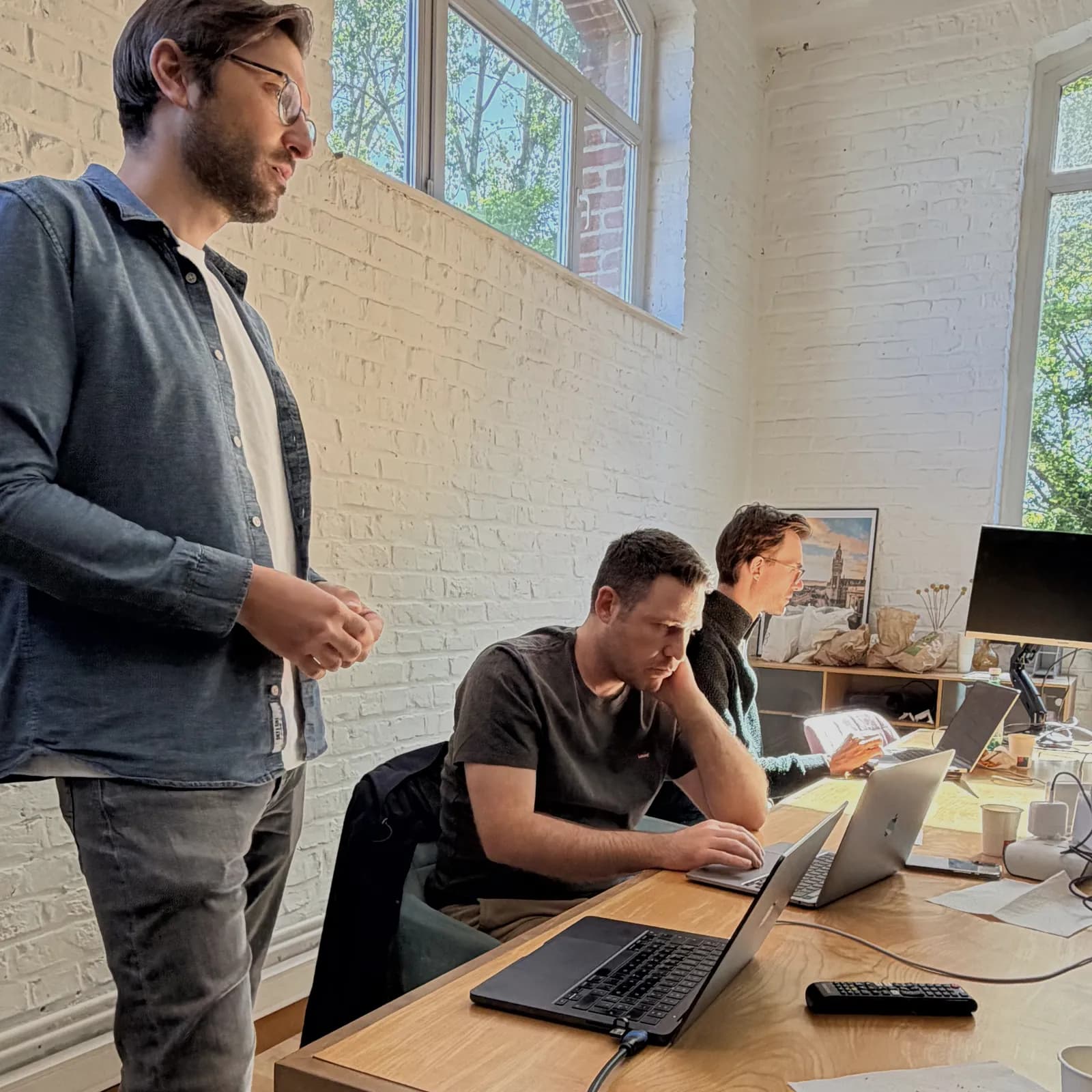 Échange debout entre un formateur Hoko et deux développeurs concentrés sur leurs écrans.