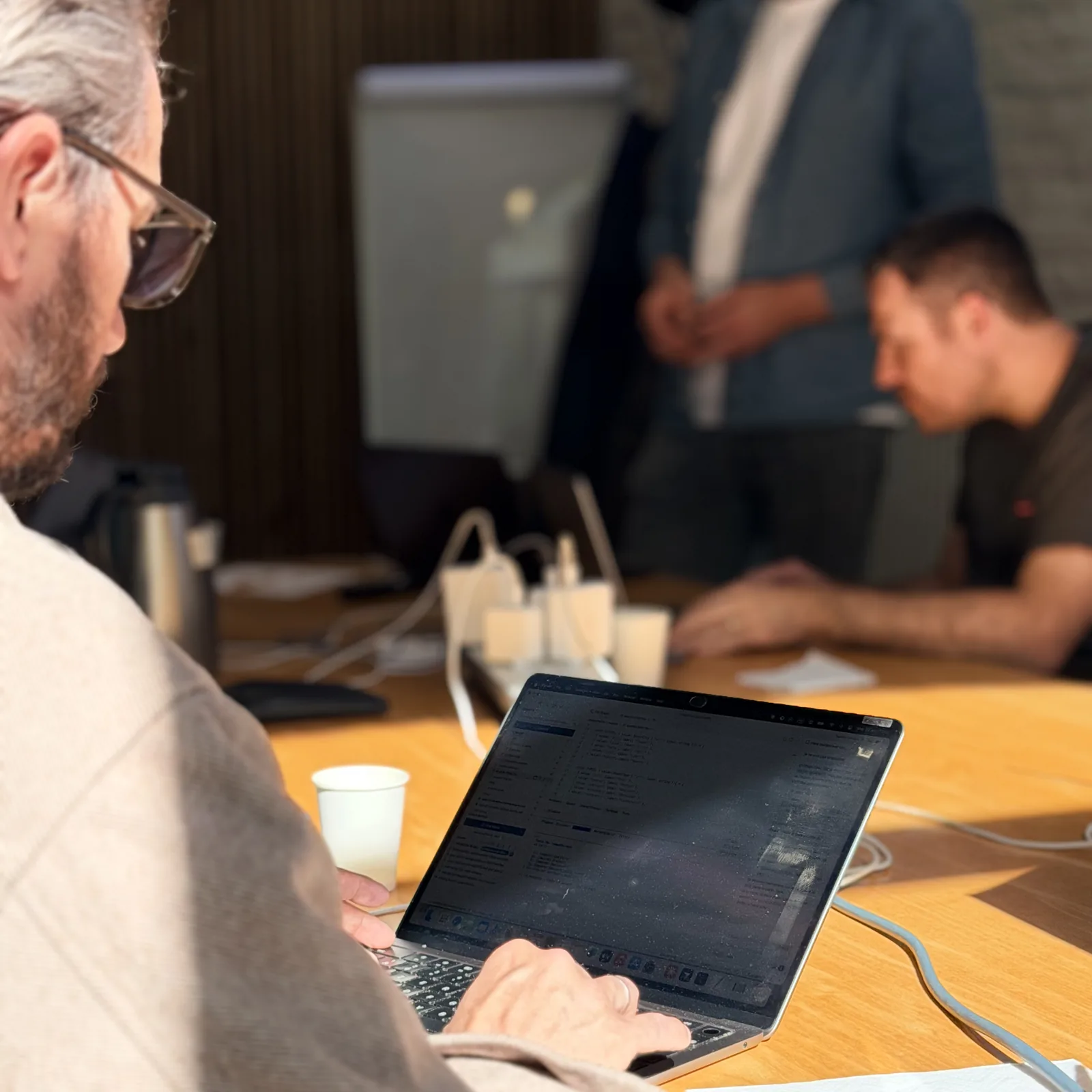 Atelier Hoko : un participant code sur son ordinateur portable au premier plan, pendant qu'un formateur accompagne un développeur à l'arrière-plan.